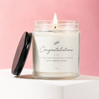 Glass candle with lit wick, black lid beside it, saying "Congratulations"