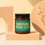 Amber candle with teal label saying "Surviving Wedding Season" with "Vowed" below.