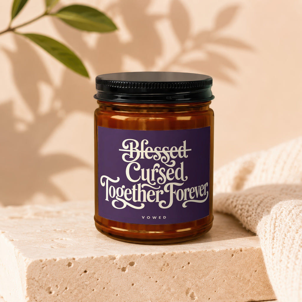 Amber candle with purple label reading "Blessed Cursed Together Forever" above "vowed".