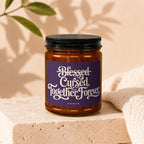 Amber candle with purple label reading "Blessed Cursed Together Forever" above "vowed".