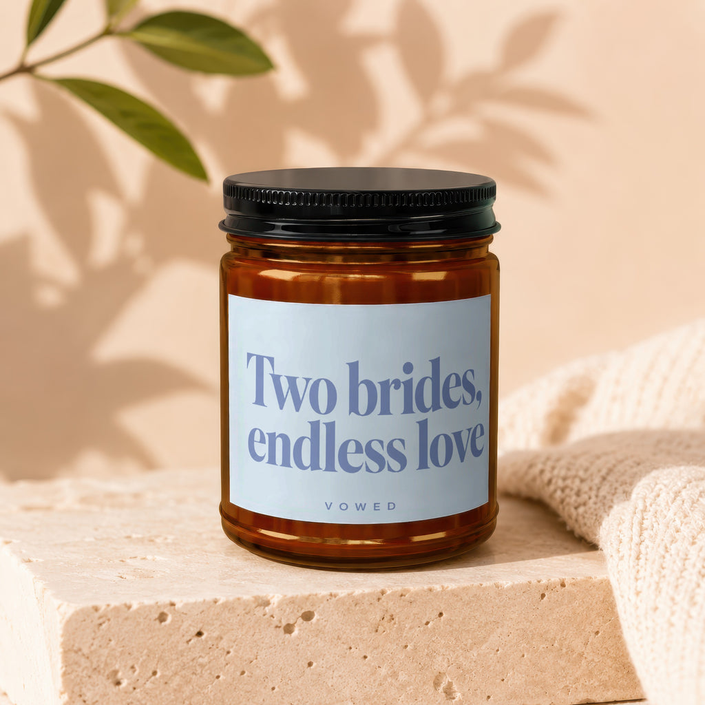 Candle with "Two brides, endless love" text on label, on textured block.