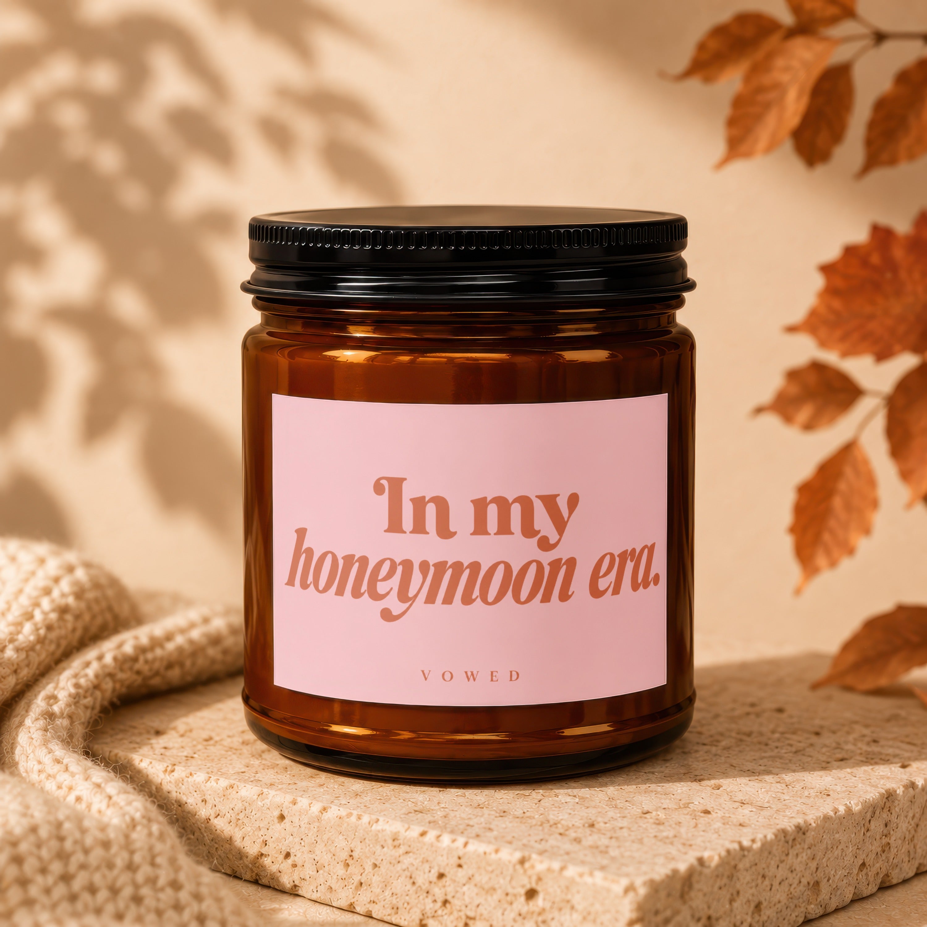 Amber jar candle with pink label reading "In my honeymoon era. VOWED."
