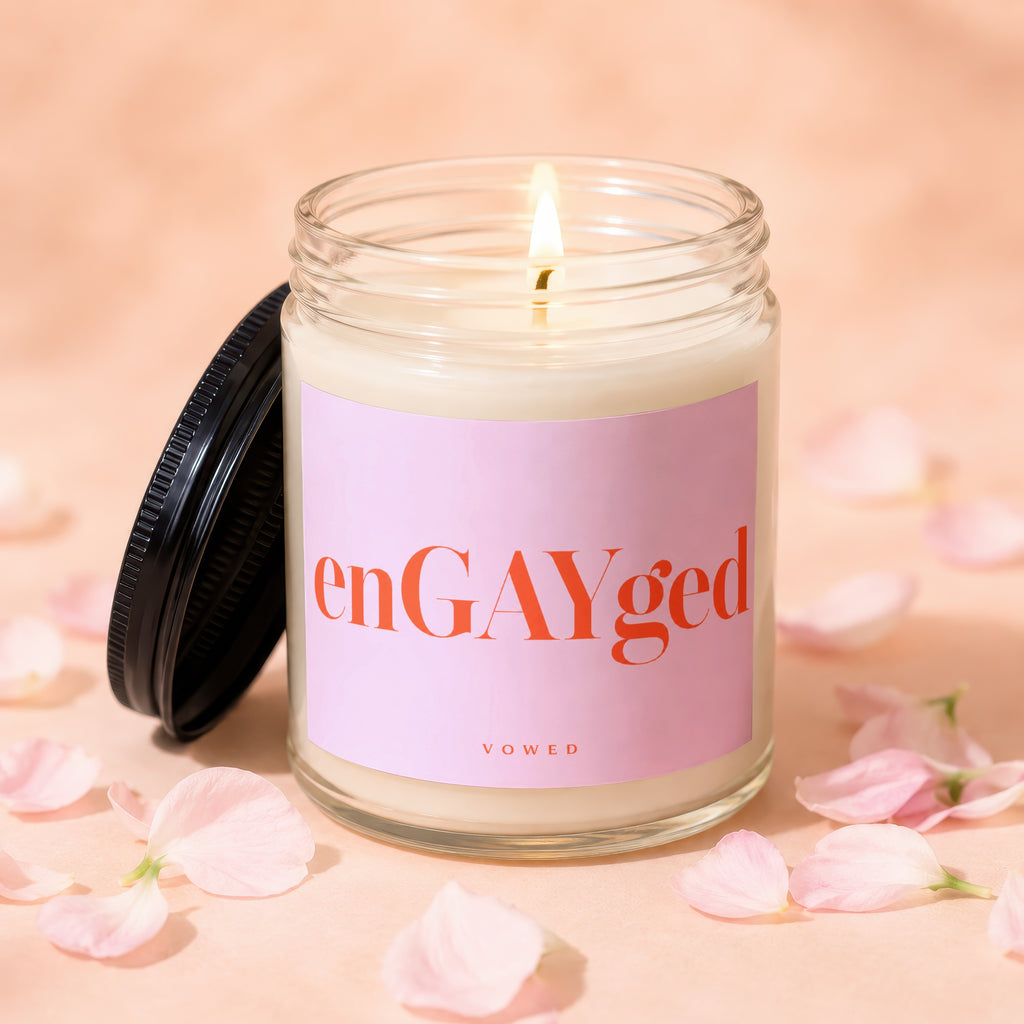 Glass candle with flickering flame, light pink label reads "enGAYged" and "VOWED".