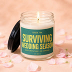 Candle with "Surviving Wedding Season" text, lid to the side, surrounded by pink petals.
