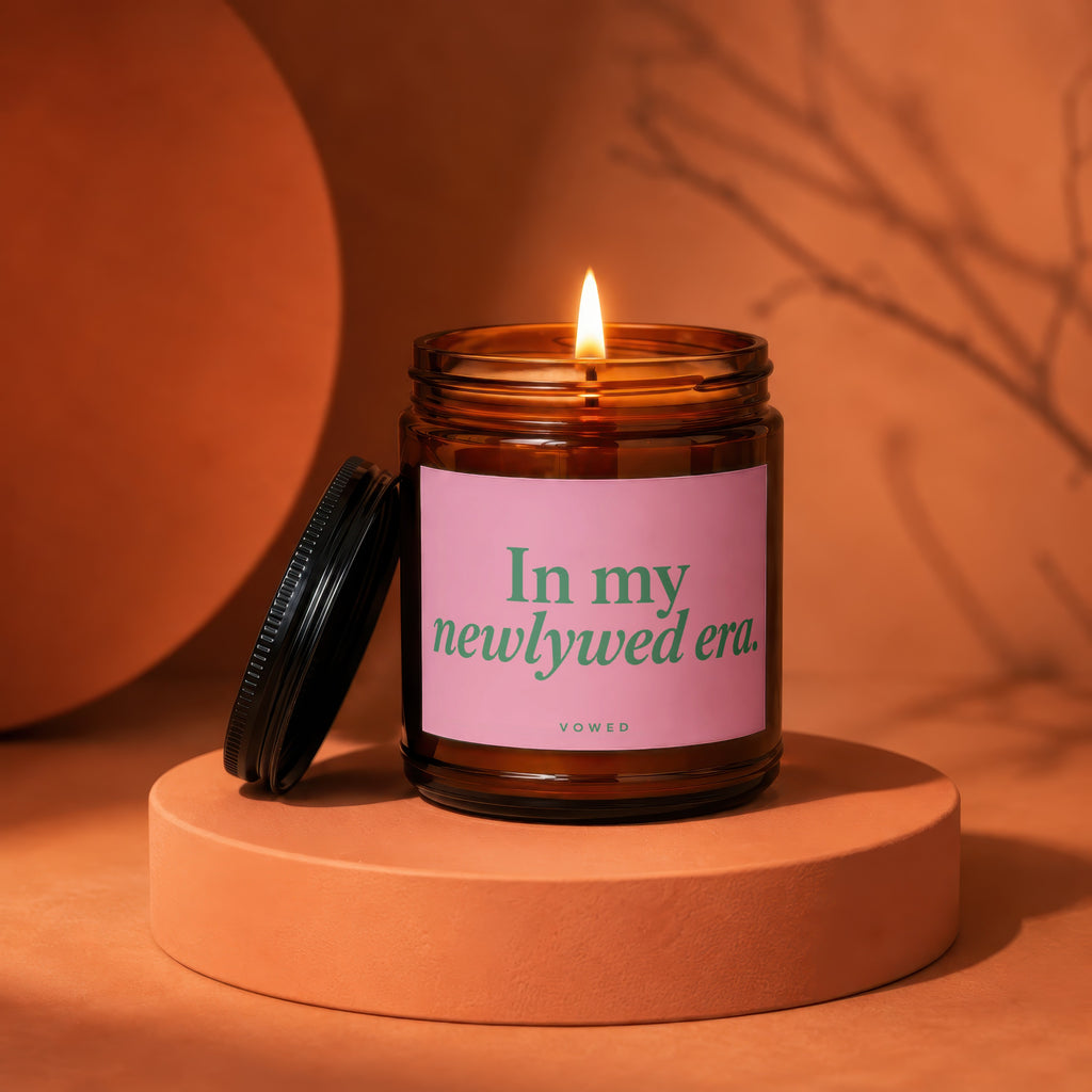 Amber jar candle with pink label reading "In my newlywed era." Vowed.