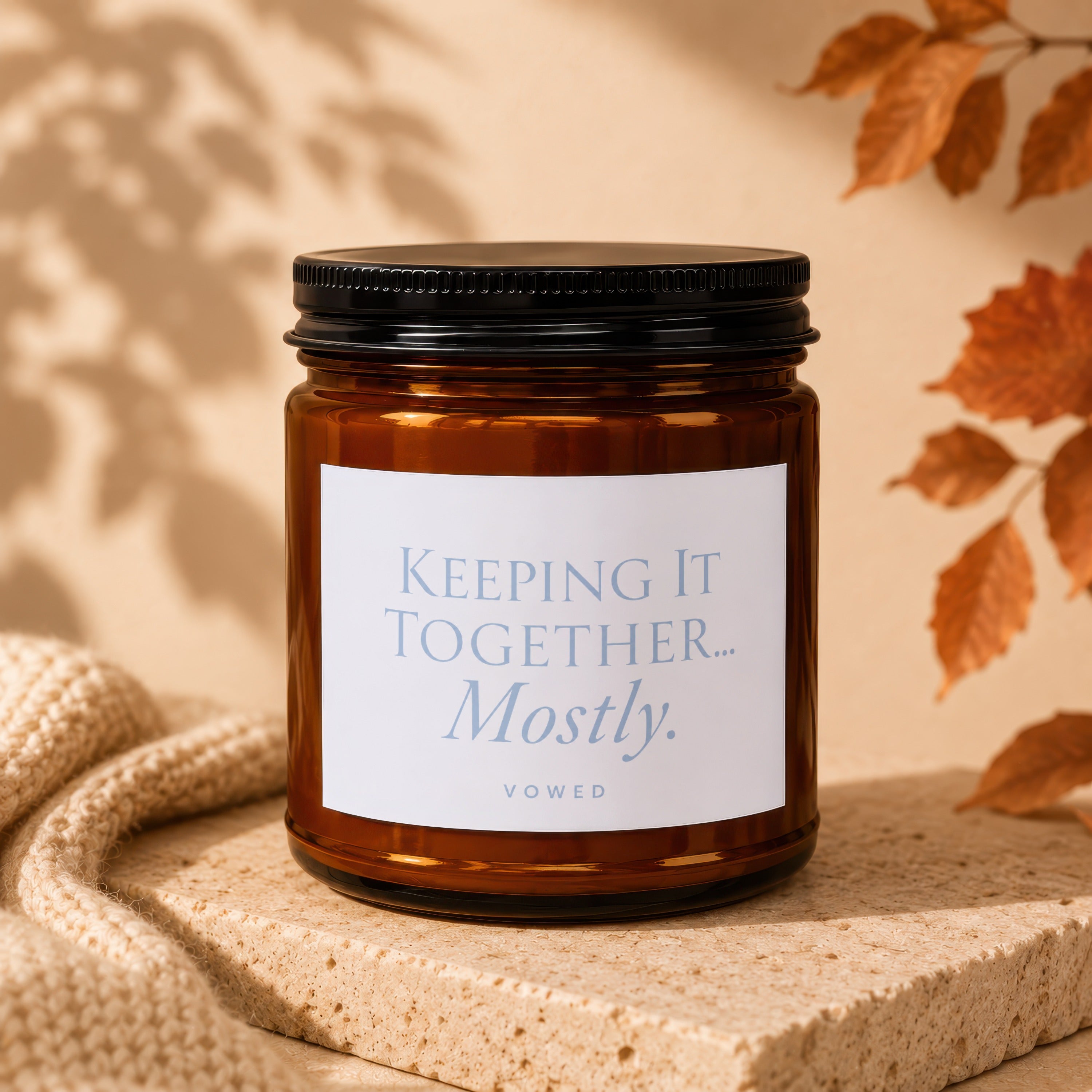 Brown glass candle with black lid, label reads "Keeping It Together... Mostly. VOWED".