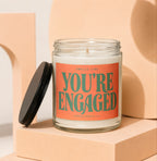 Glass candle with orange label reading "Smells Like You're Engaged"
