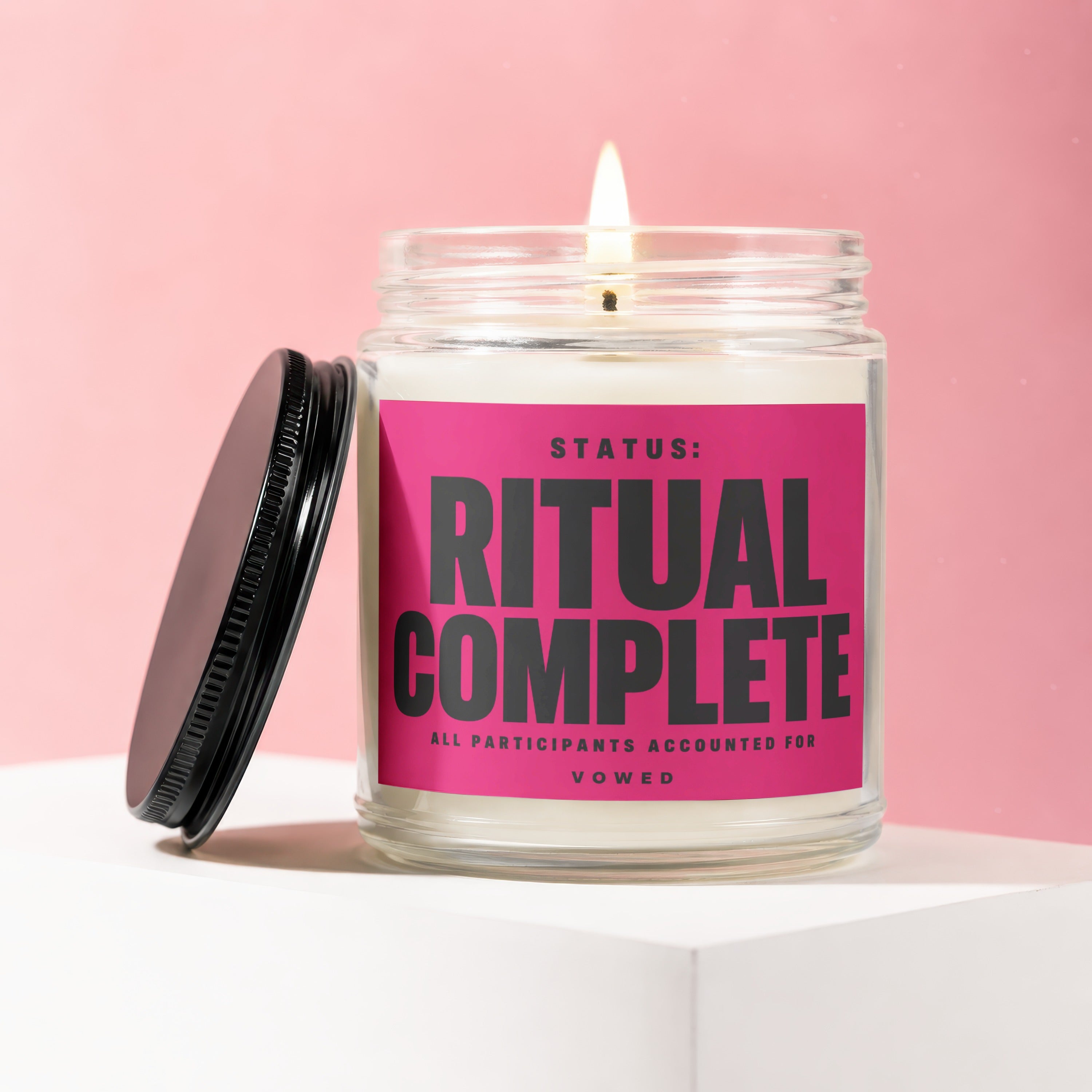 Jar candle with lit wick and pink label reading "RITUAL COMPLETE".