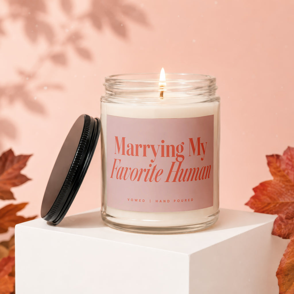 Candle with text "Marrying My Favorite Human" on a pink background with autumn leaves.