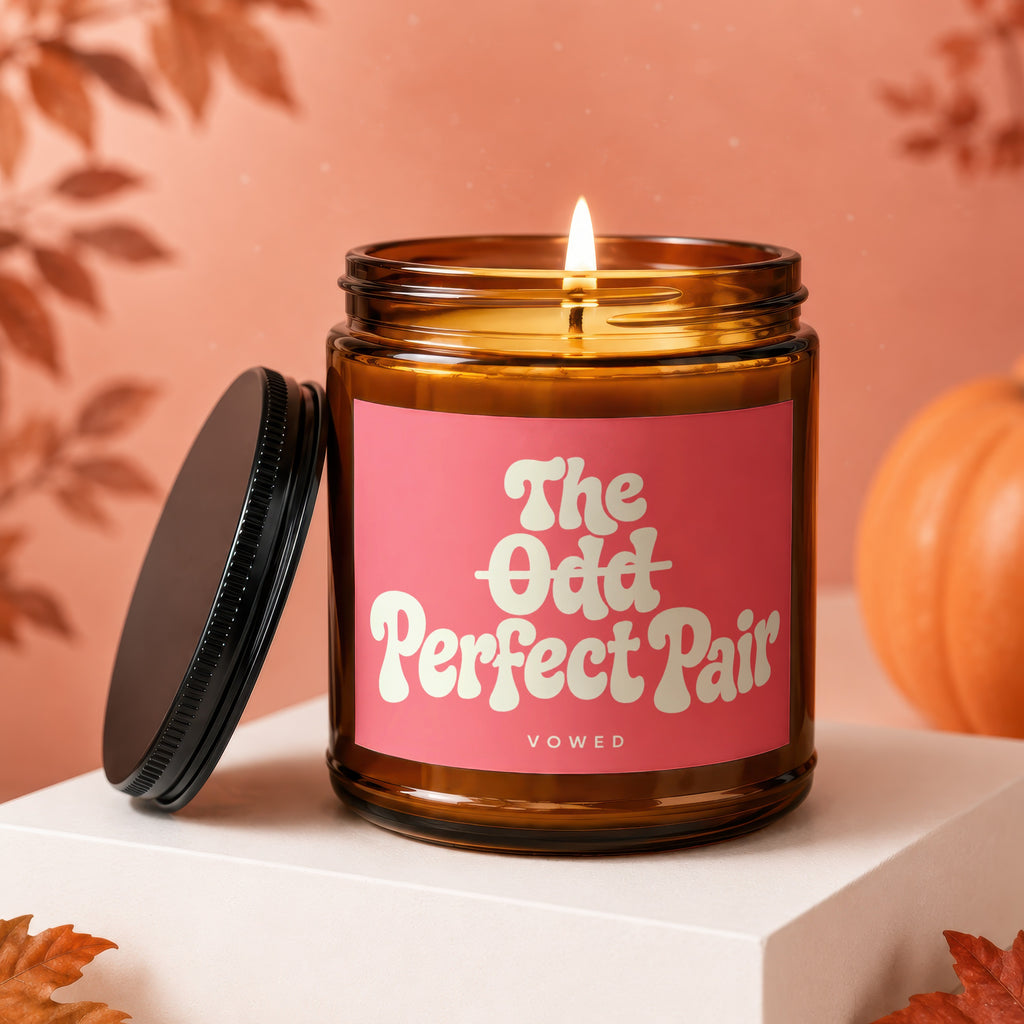 Amber glass candle with pink label reading "The Odd Perfect Pair VOWED."
