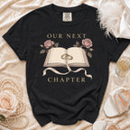 Black t-shirt with "Our Next Chapter" text, open book, rings, and roses design.