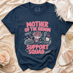 Navy t-shirt with "Mother of the Groom Support Squad" graphic, clutch, flowers, and champagne.