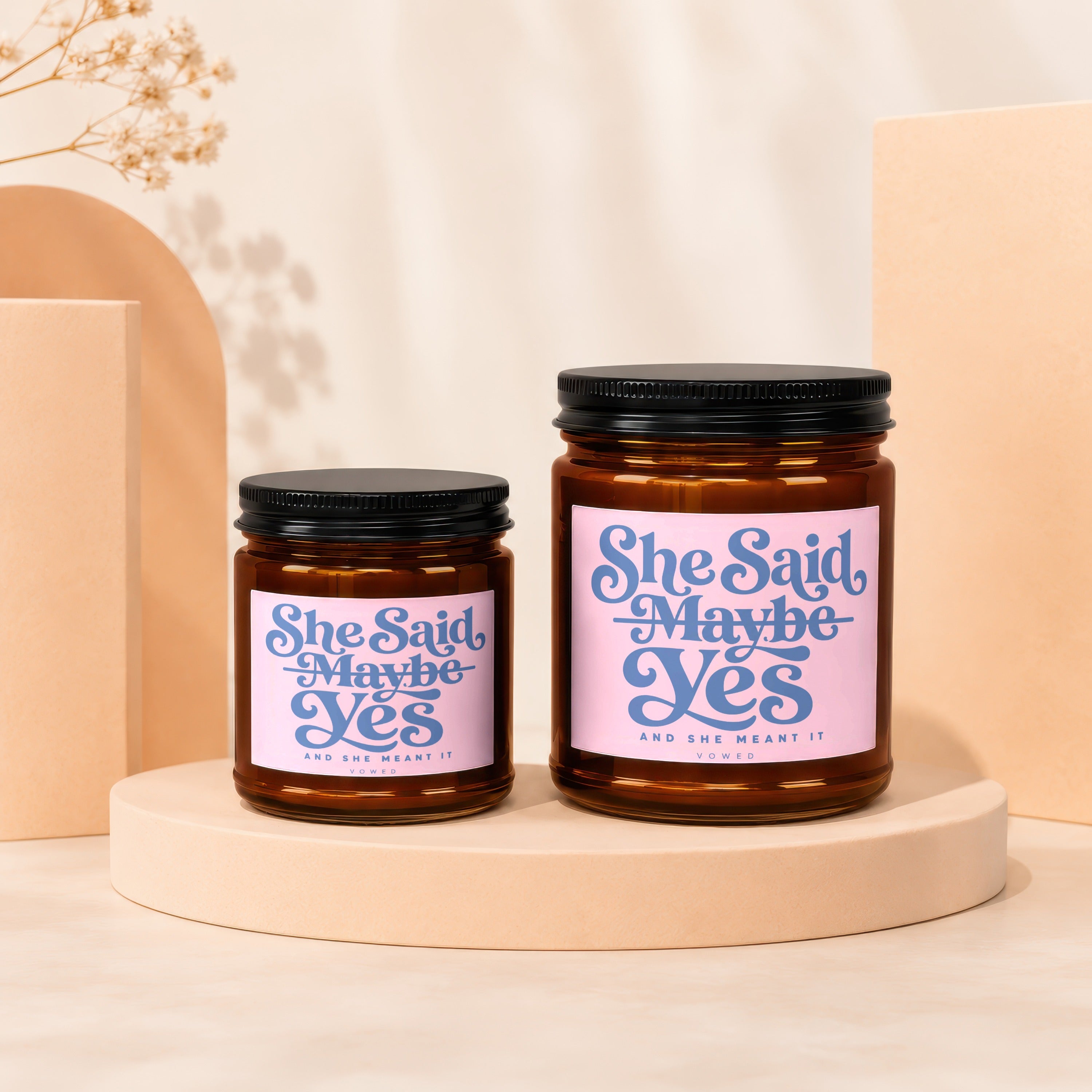 Two amber glass candles with pink labels reading "She Said Maybe Yes" and "And She Meant It".