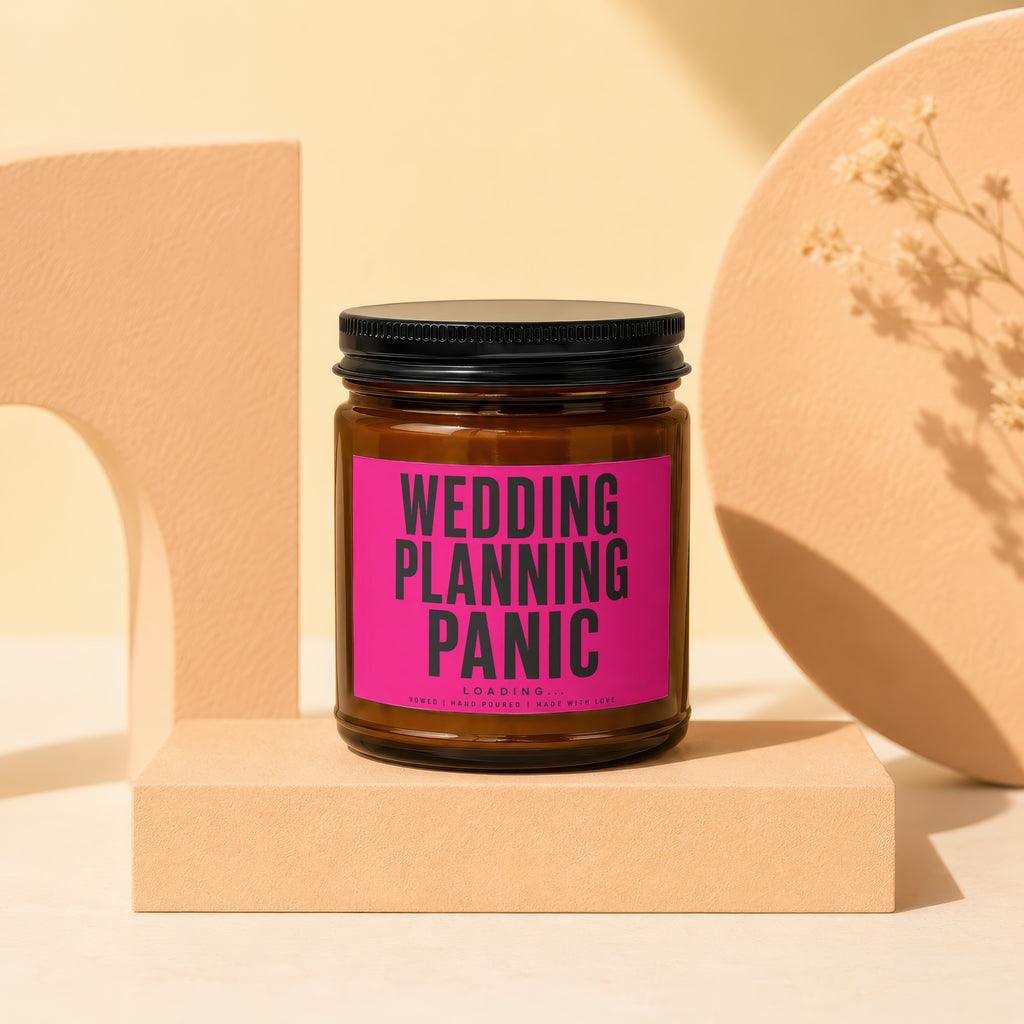 Glass jar candle with "WEDDING PLANNING PANIC LOADING..." pink label on display stand.