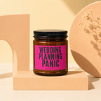 Glass jar candle with "WEDDING PLANNING PANIC LOADING..." pink label on display stand.