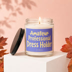 Lit candle in glass jar with "Amateur Professional Dress Holder" label on a white display cube.
