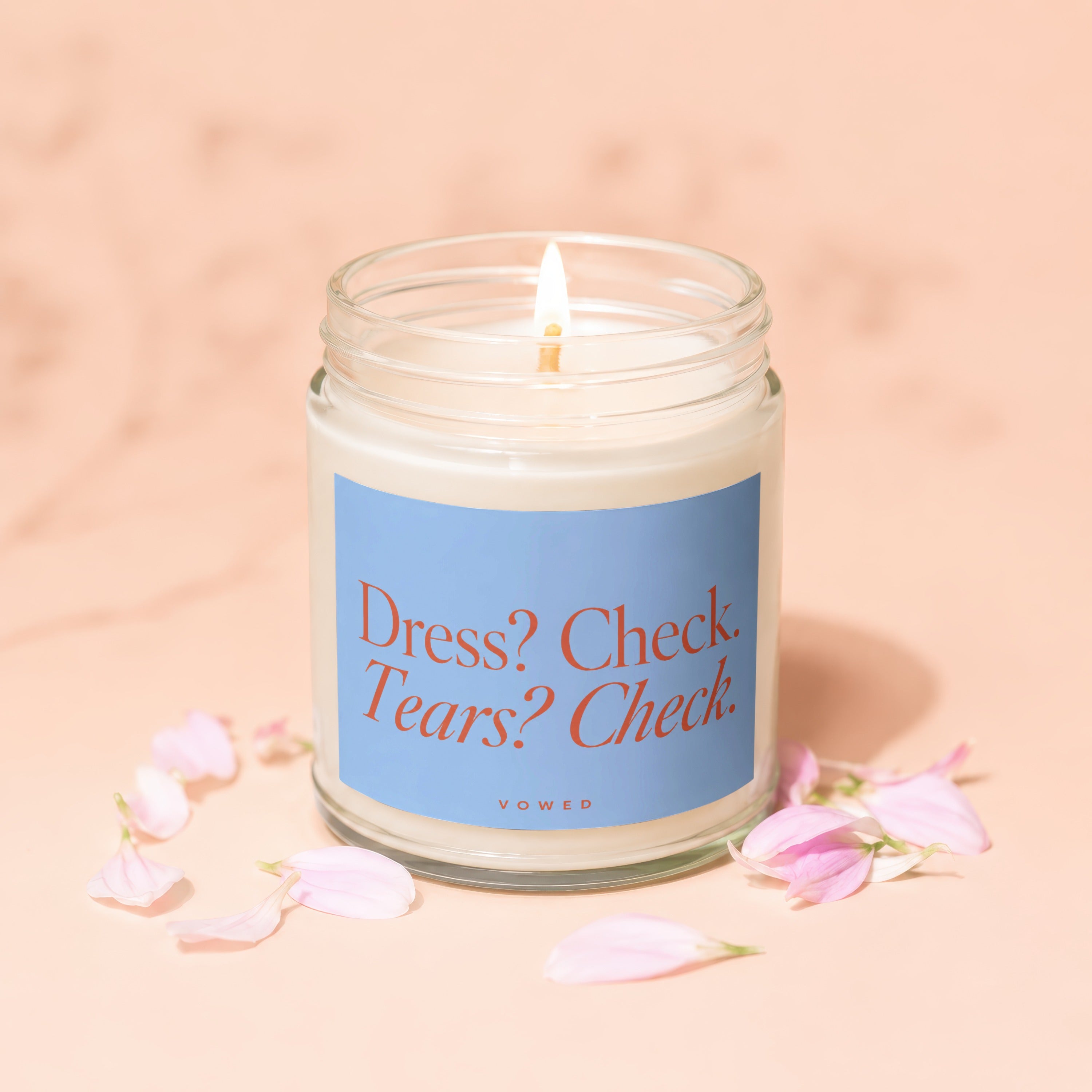 Candle with "Dress? Check. Tears? Check." text on blue label, surrounded by petals.