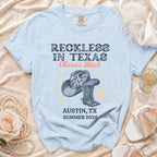 Light blue t-shirt with "Reckless in Texas Olivia's Bach Austin, TX Summer 2026" text.