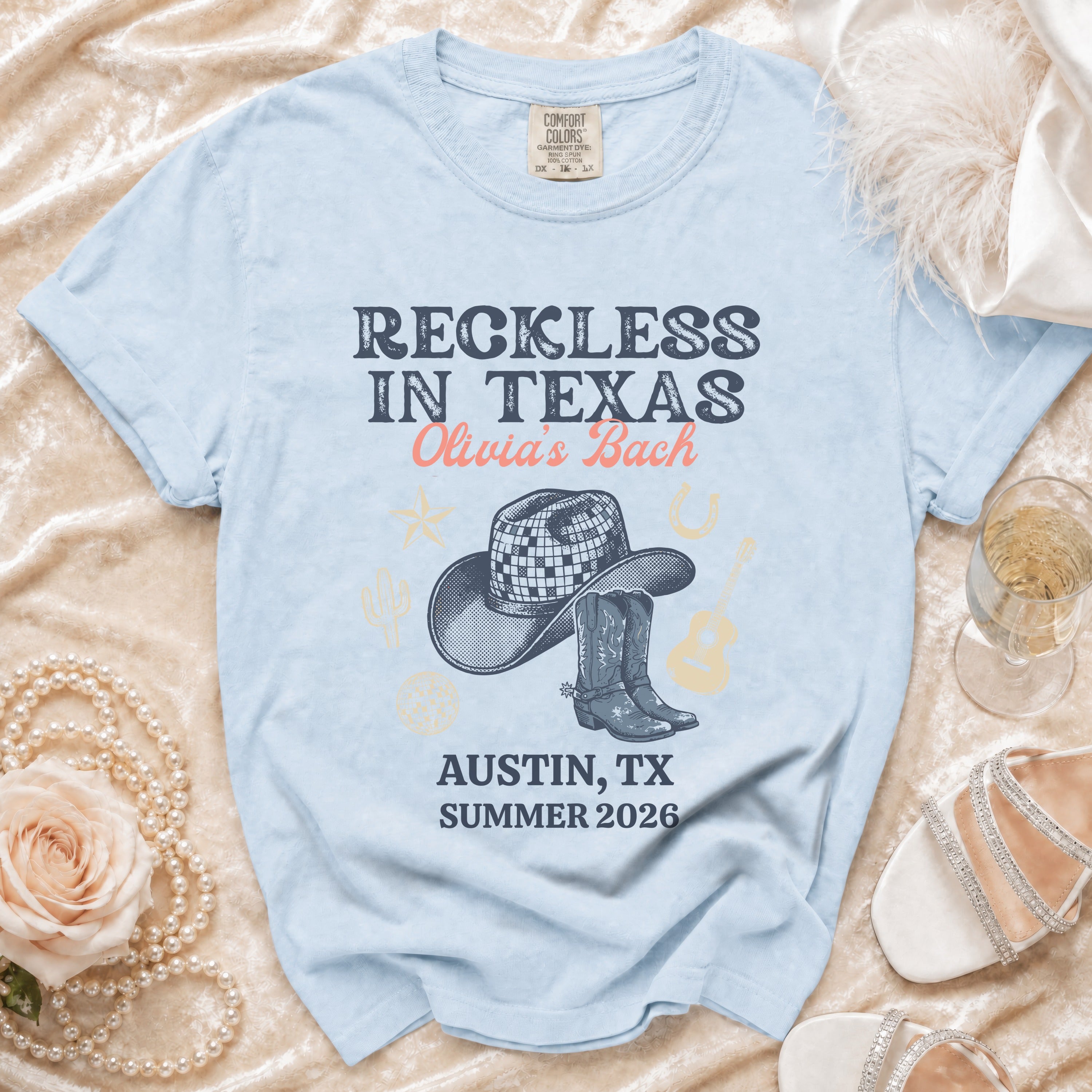 Light blue t-shirt with "Reckless in Texas Olivia's Bach Austin, TX Summer 2026" text.