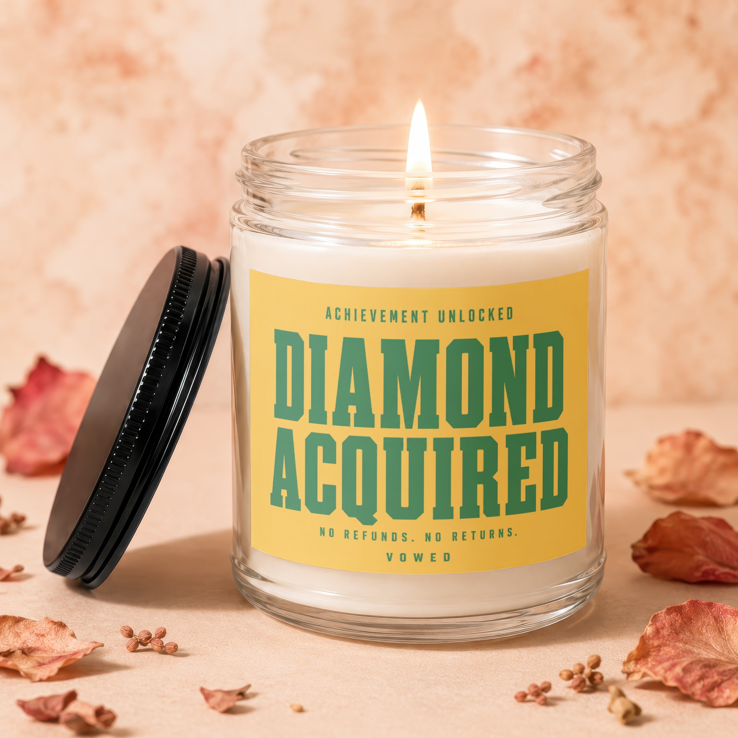Glass jar candle with lit wick, reads "DIAMOND ACQUIRED NO REFUNDS. NO RETURNS."