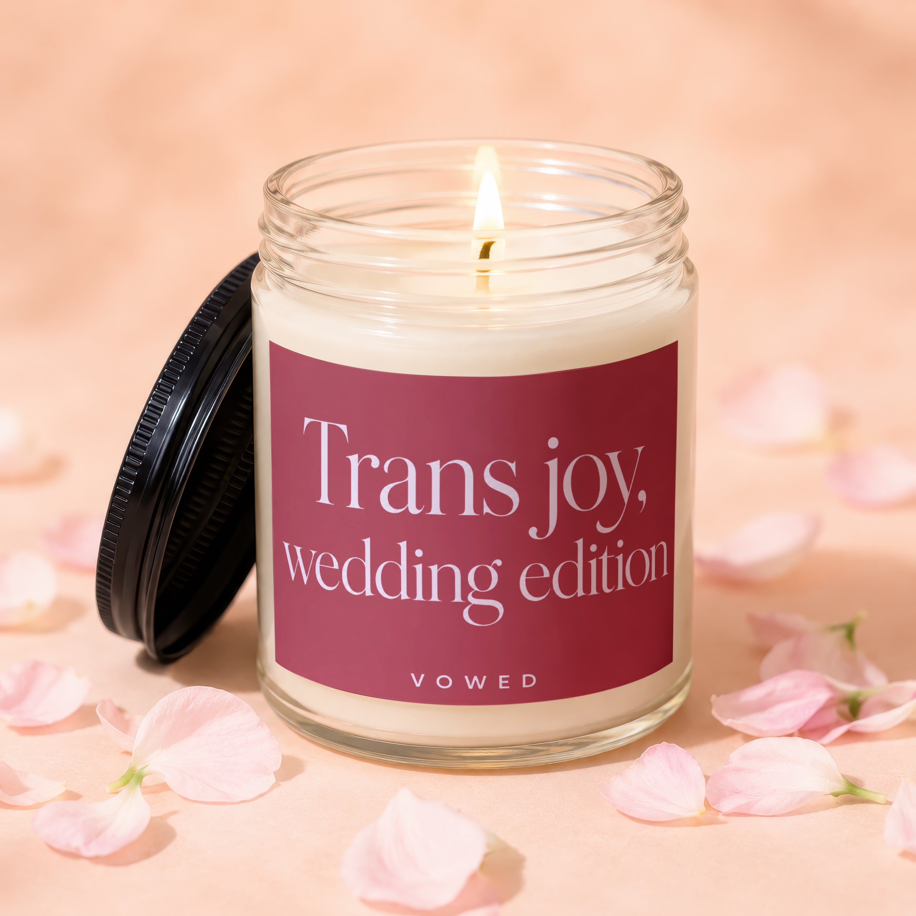 Glass candle with lit wick and dark lid, labeled "Trans joy, wedding edition"