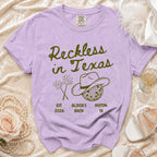 Lilac t-shirt with "Reckless in Texas" design, cowboy hat, and fireworks.