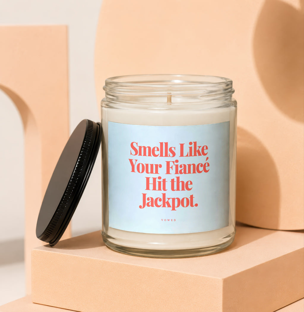 Candle with black lid and label reading "Smells Like Your Fiancé Hit the Jackpot. VOWED."