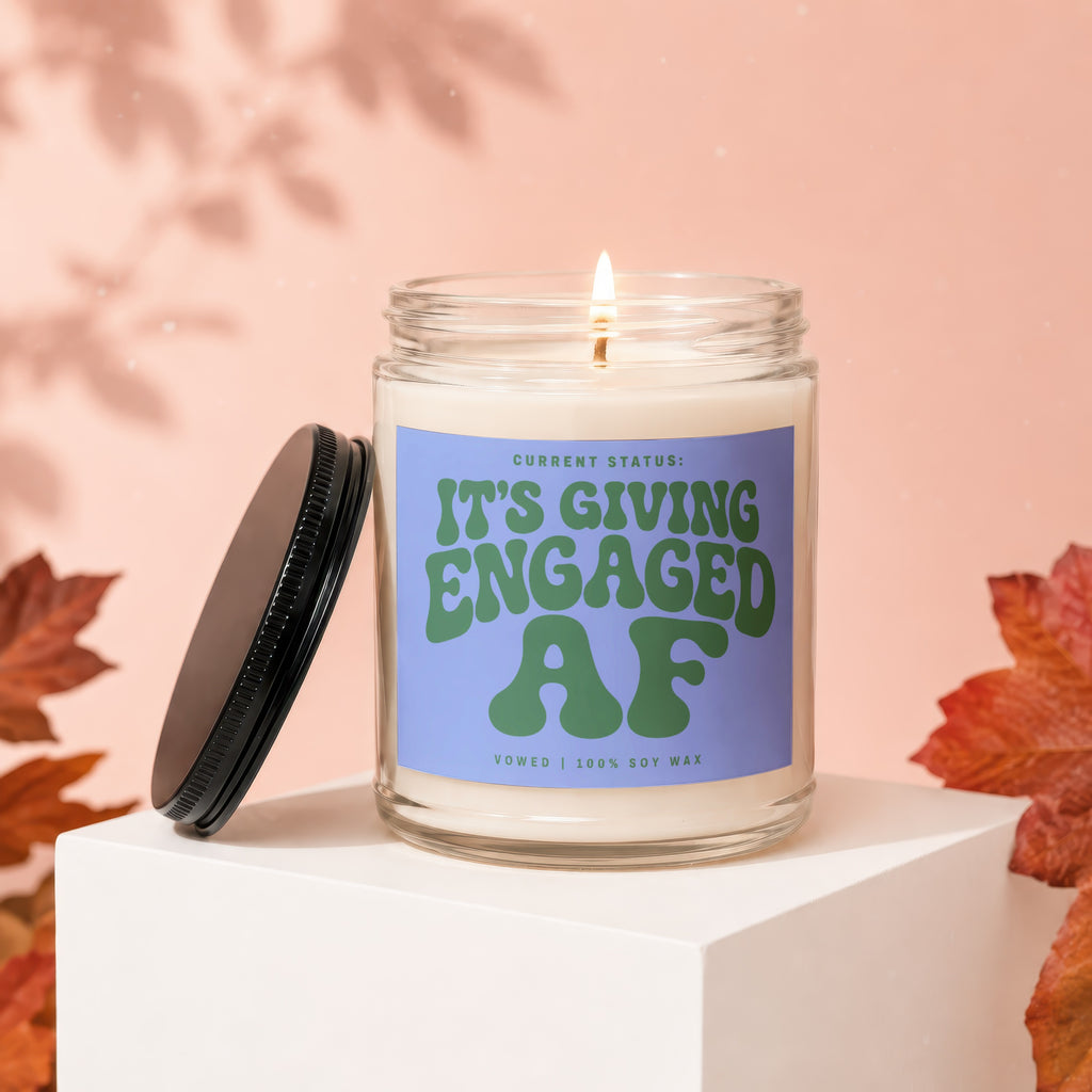 Glass candle with a lit wick and a label that reads "It's Giving Engaged AF".