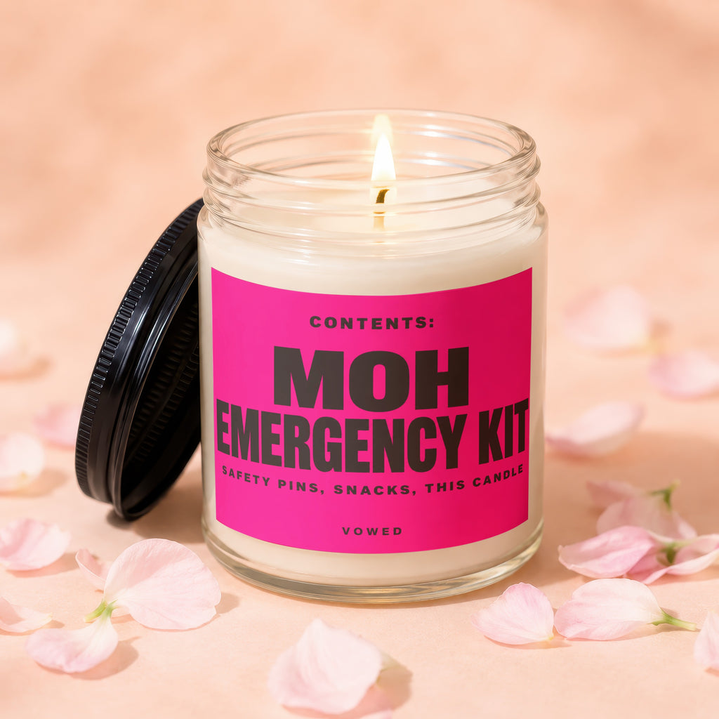 Glass candle with lit wick, pink label reads "MOH EMERGENCY KIT."