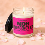 Glass candle with lit wick, pink label reads "MOH EMERGENCY KIT."