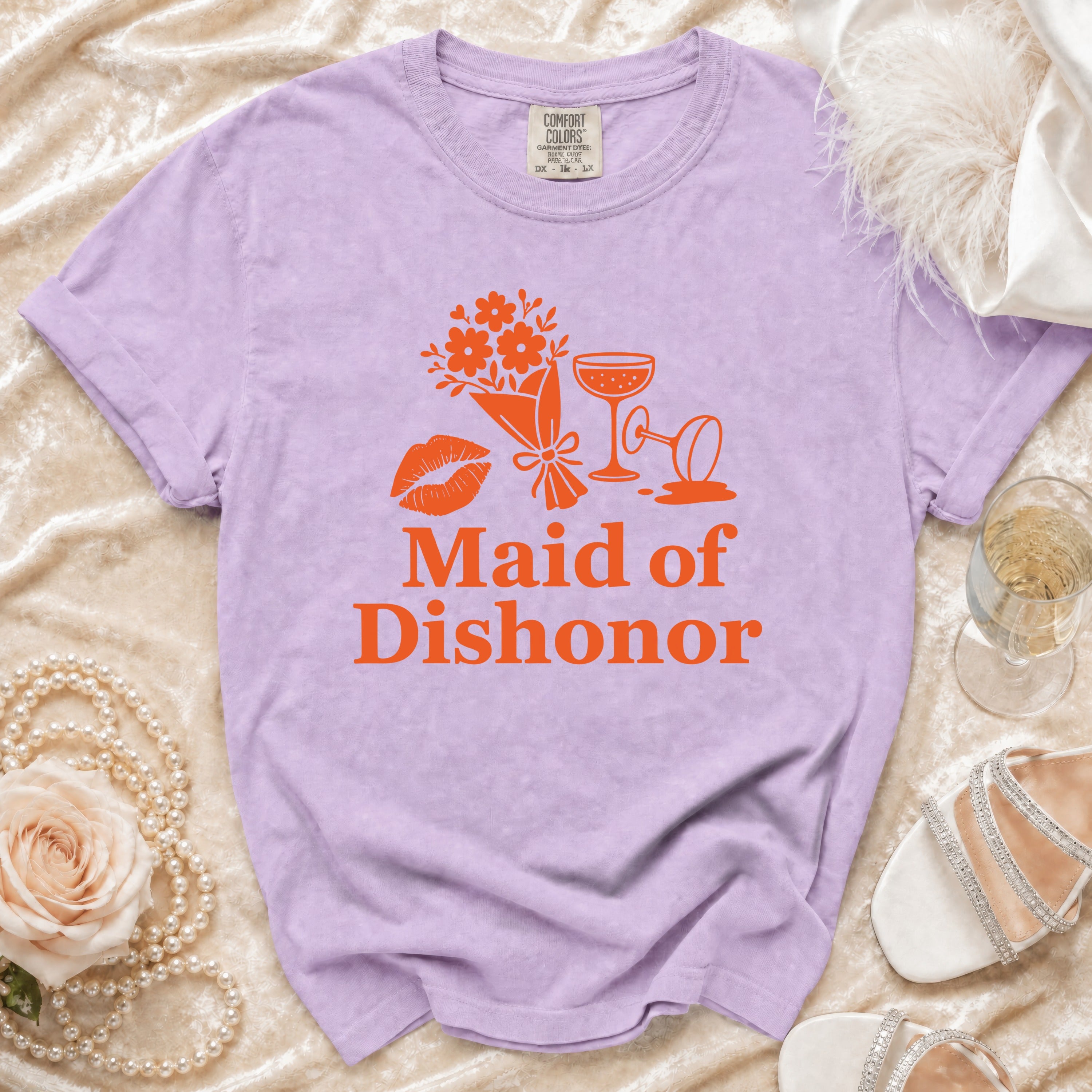 Purple t-shirt with orange text "Maid of Dishonor," lips, flowers, and champagne glasses.
