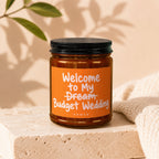 Candle with orange label reading "Welcome to My Dream Budget Wedding".
