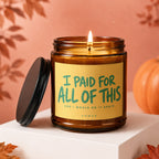 Amber candle with lit wick, yellow label text "I PAID FOR ALL OF THIS".