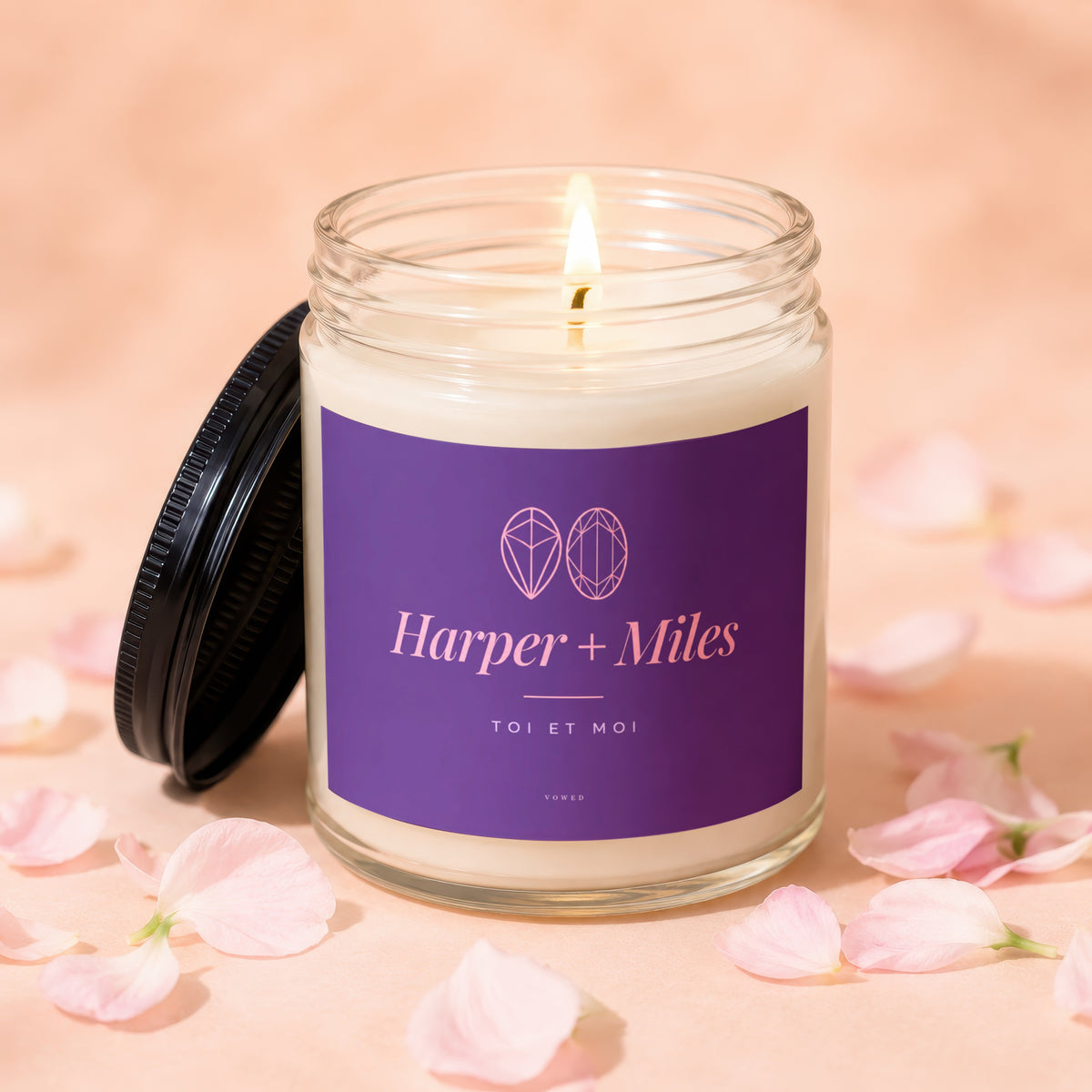 Harper + Miles candle with lid off and flame lit, surrounded by pink petals.