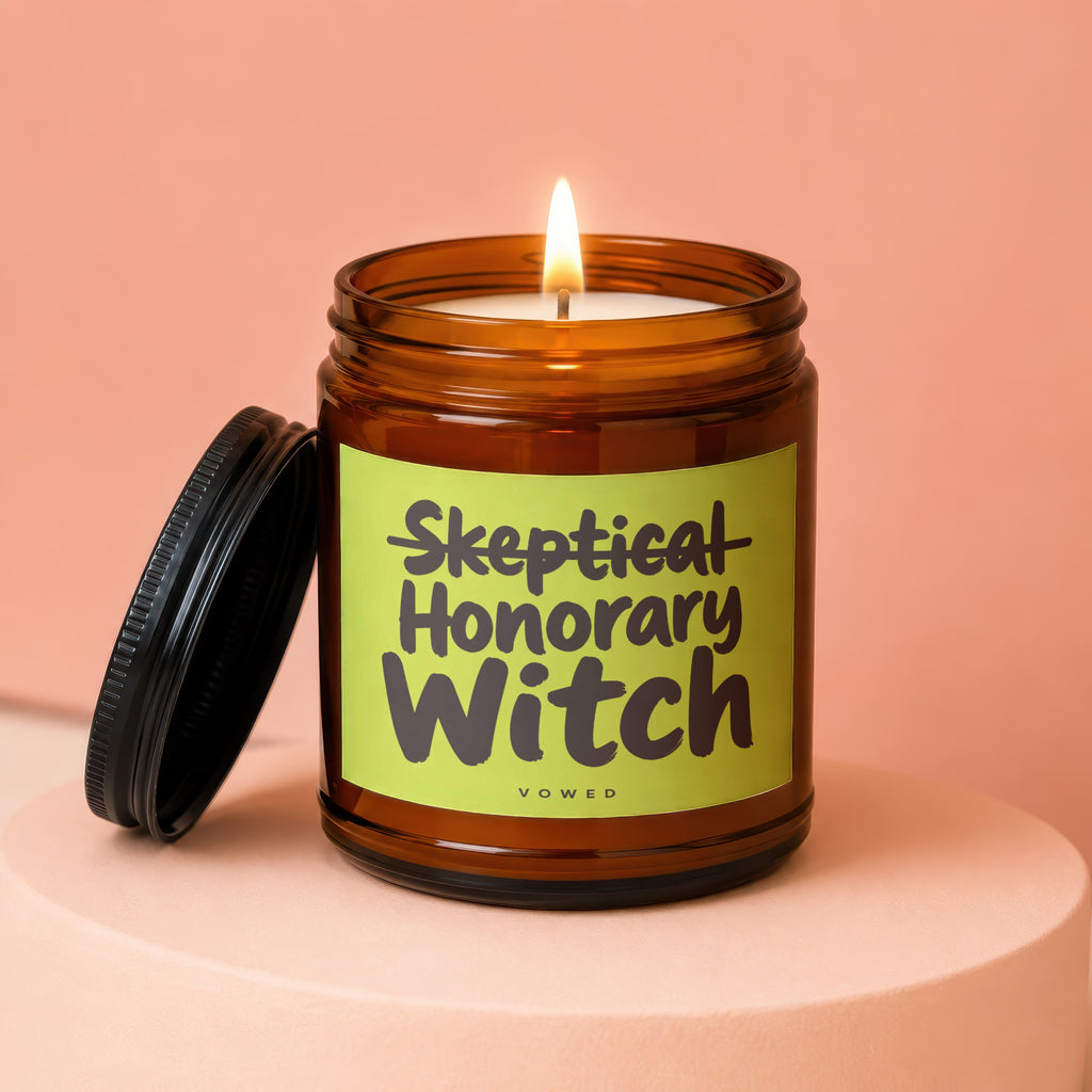 Skeptical Honorary Witch candle in amber jar with lid and lit wick.