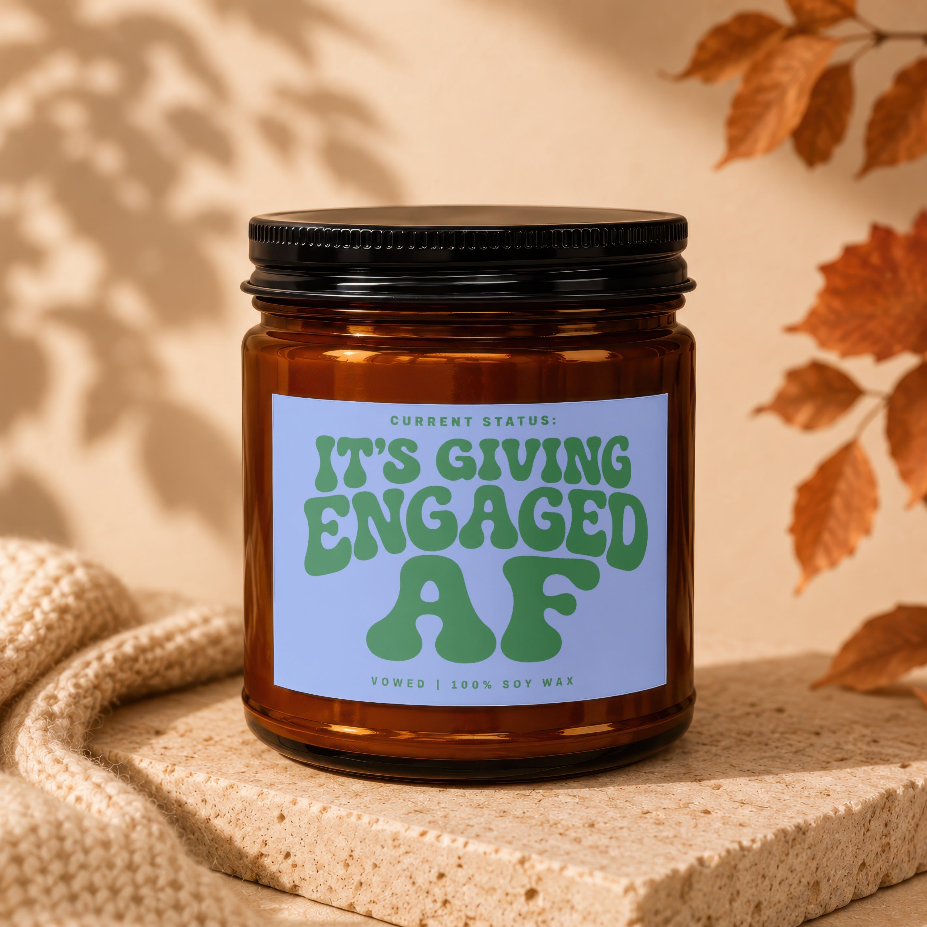 Amber jar candle with light blue label reading "CURRENT STATUS: IT'S GIVING ENGAGED AF"