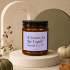Amber candle with black lid reads "Welcome to the Family. Good Luck."
