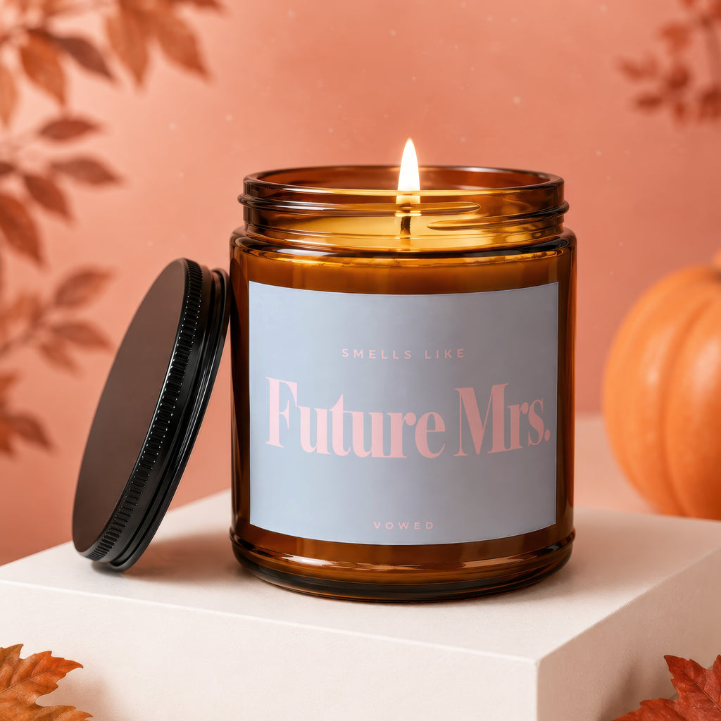 Amber glass candle with lit flame, text "Future Mrs. VOWED" on label.