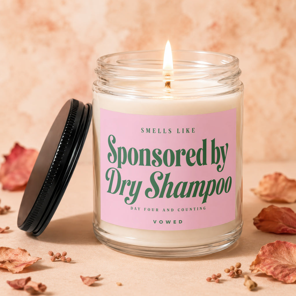 Scented candle in a glass jar with a pink label reading "Smells like Sponsored by Dry Shampoo".