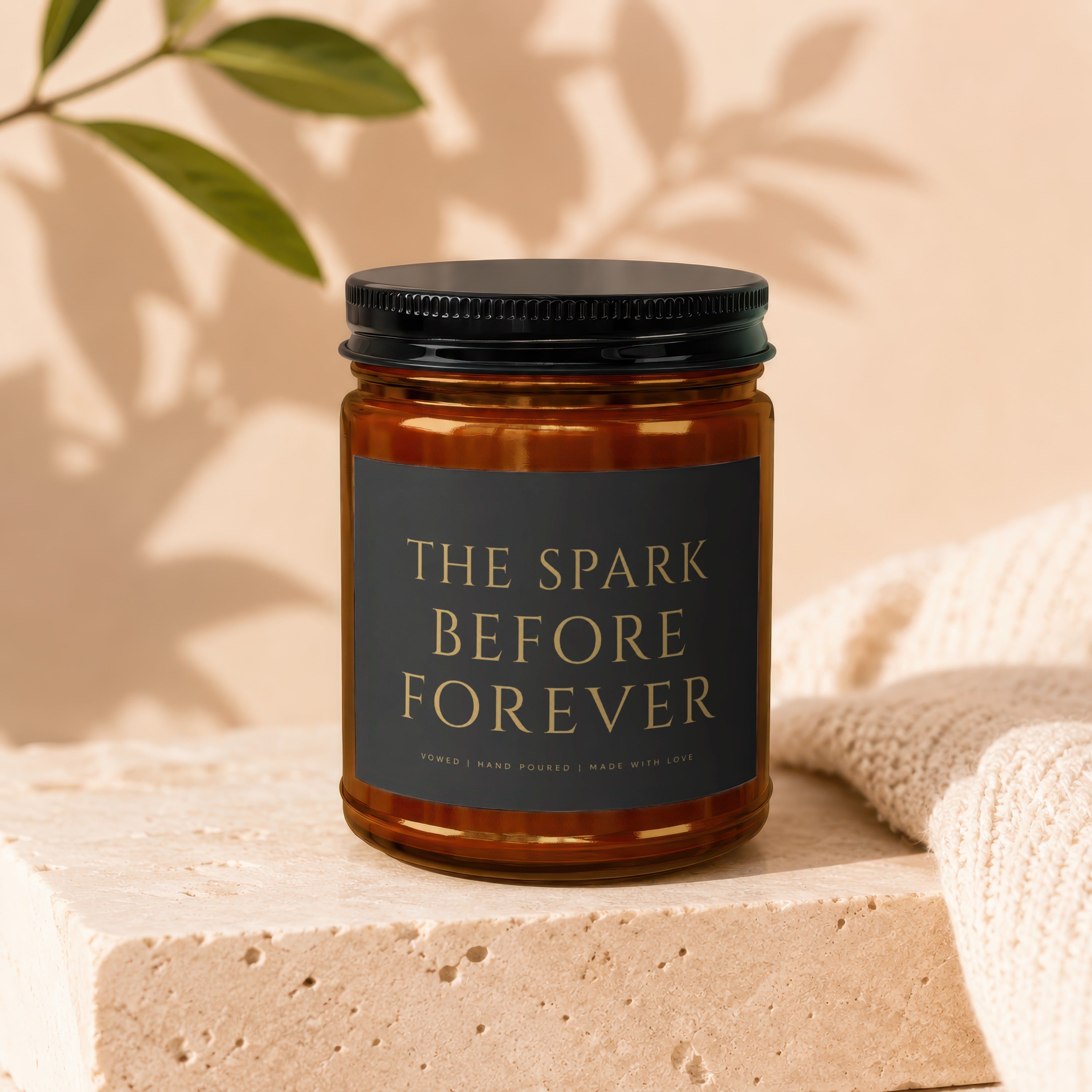 Amber glass candle with black label reading "THE SPARK BEFORE FOREVER."