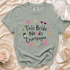 This Bride Needs Champagne graphic tee with champagne bottle and glasses.