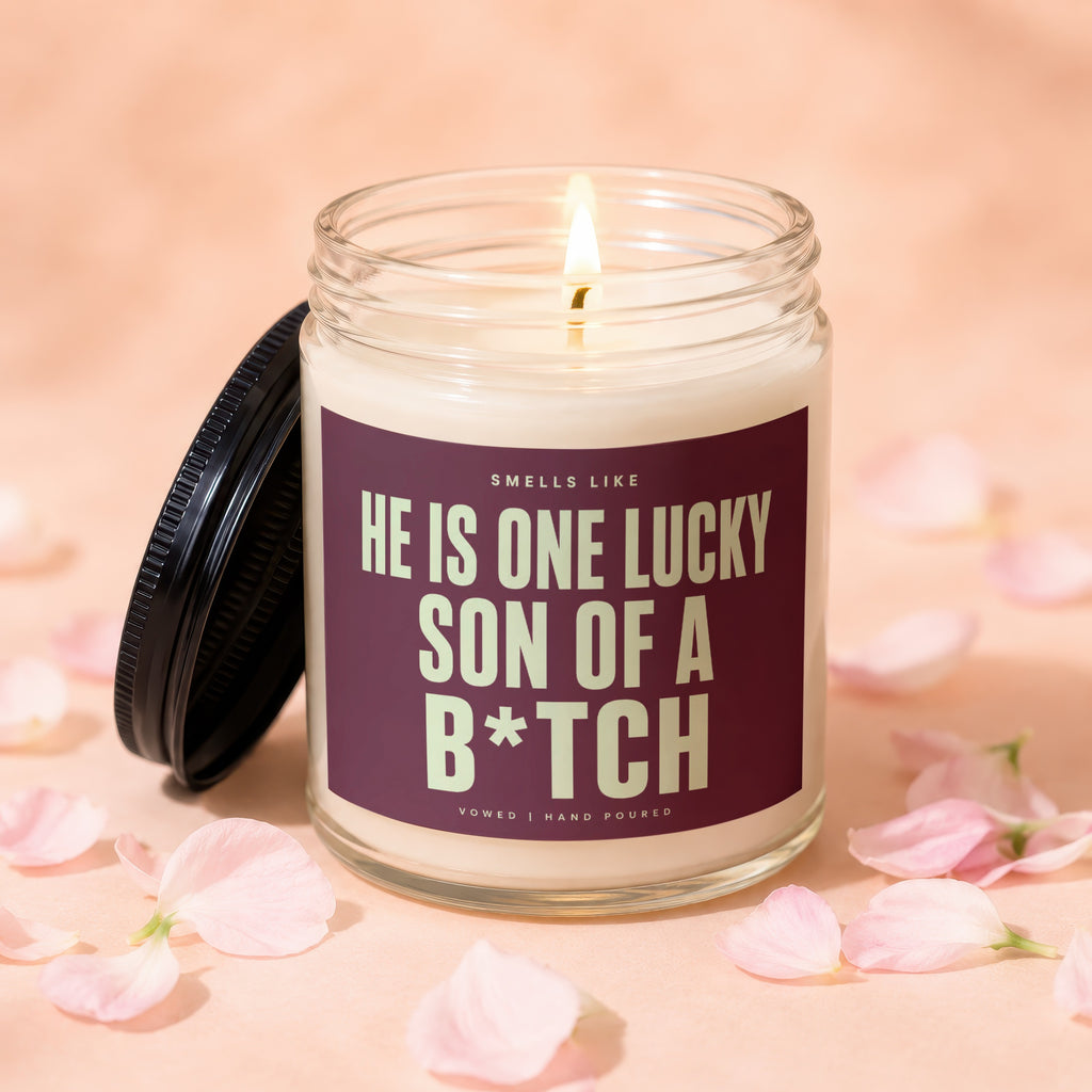 Lit candle in a glass jar with text "HE IS ONE LUCKY SON OF A B*TCH".