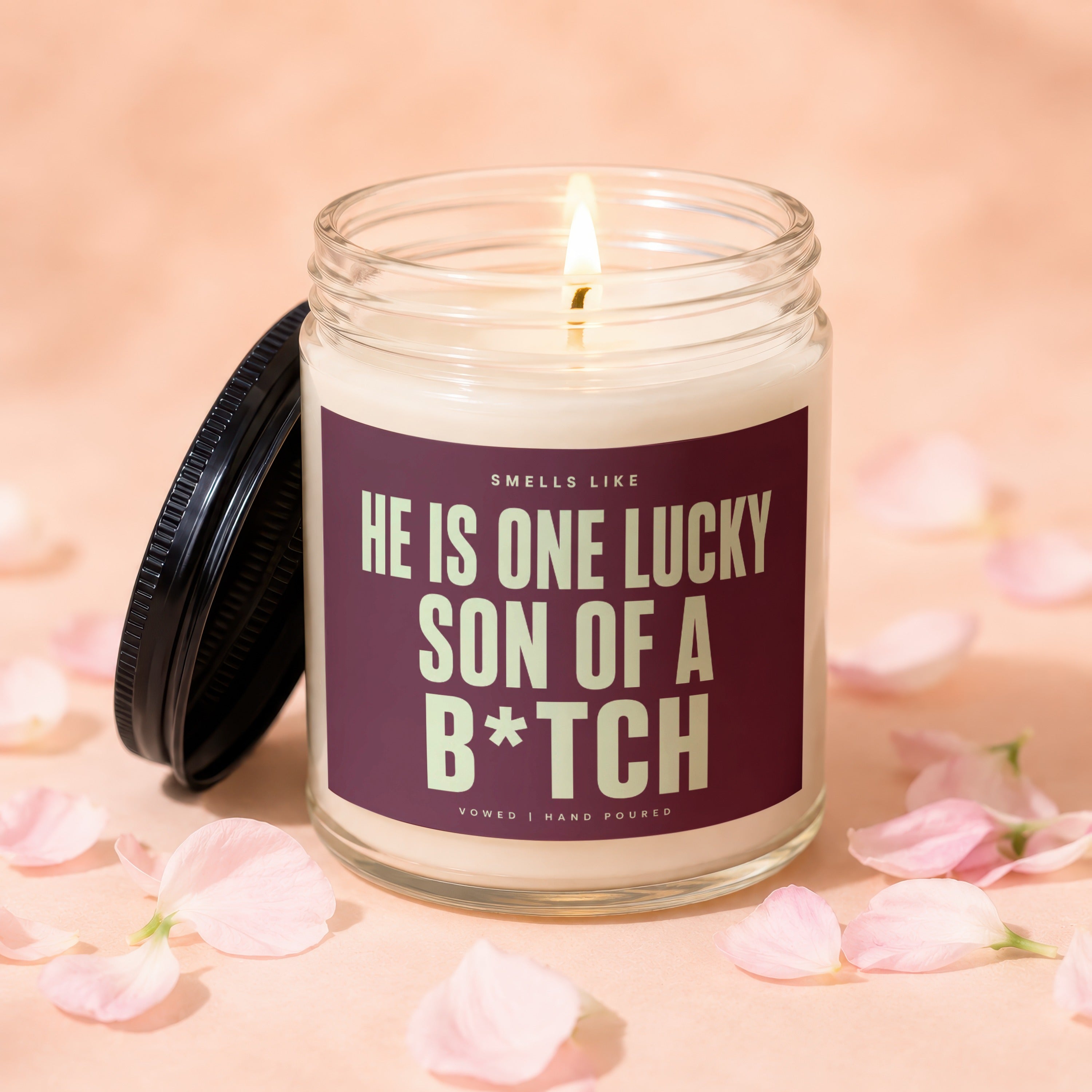 Lit candle in a glass jar with text "HE IS ONE LUCKY SON OF A B*TCH".