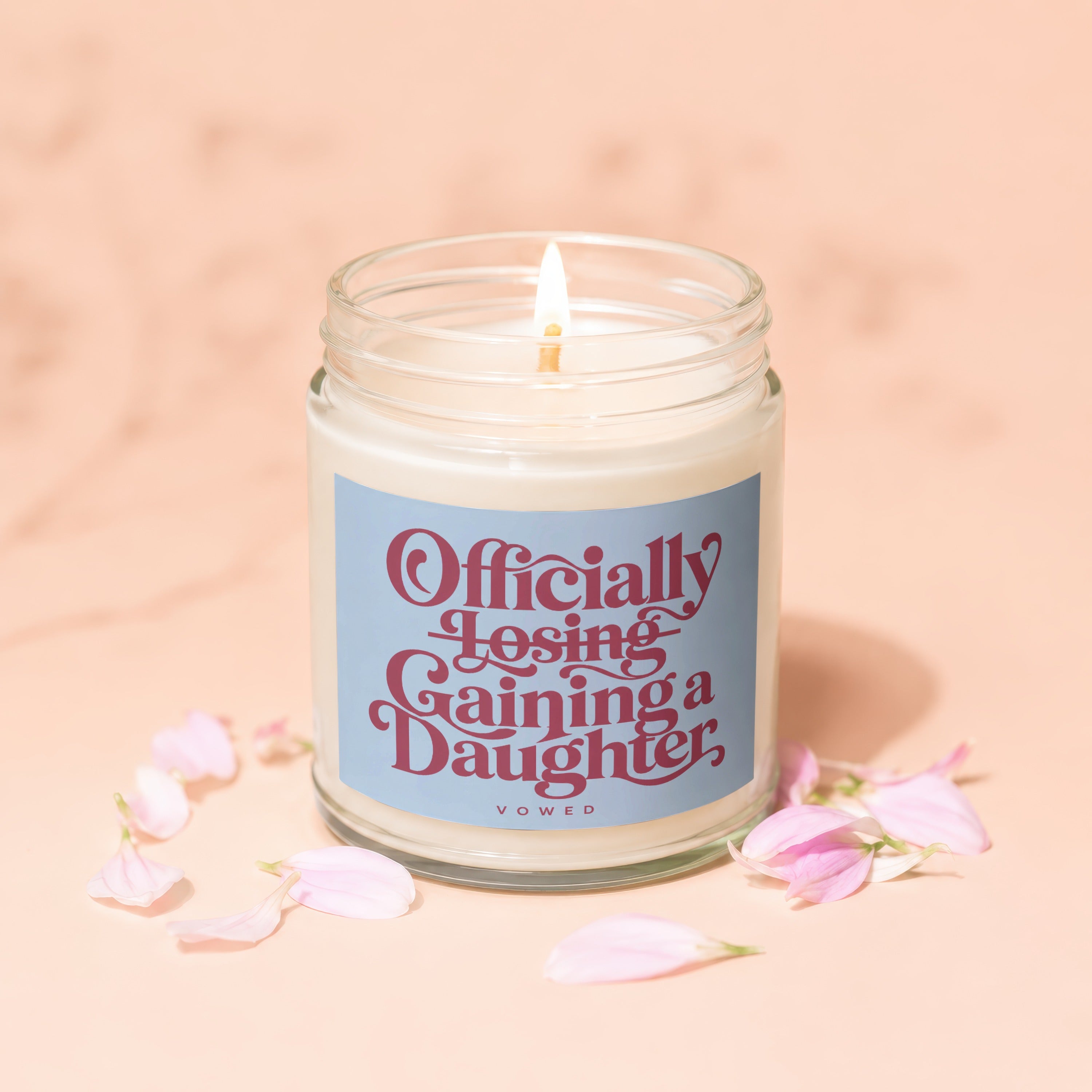 Candle with blue label reading "Officially Losing Gaining a Daughter" with petals.