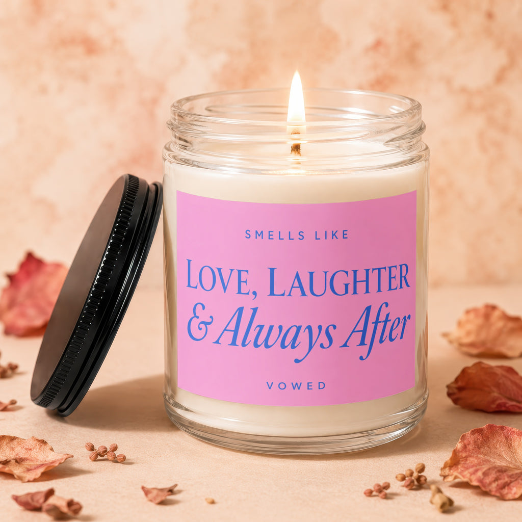 Burning candle in a glass jar with pink label reading "Smells Like Love, Laughter & Always After Vowed."