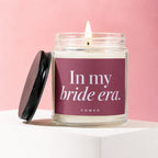 Glass candle with lit wick and black lid, reads "In my bride era."