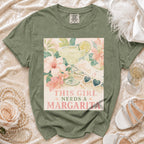 Green t-shirt with watercolor graphic of a margarita, flowers, and text "This Girl Needs a Margarita".