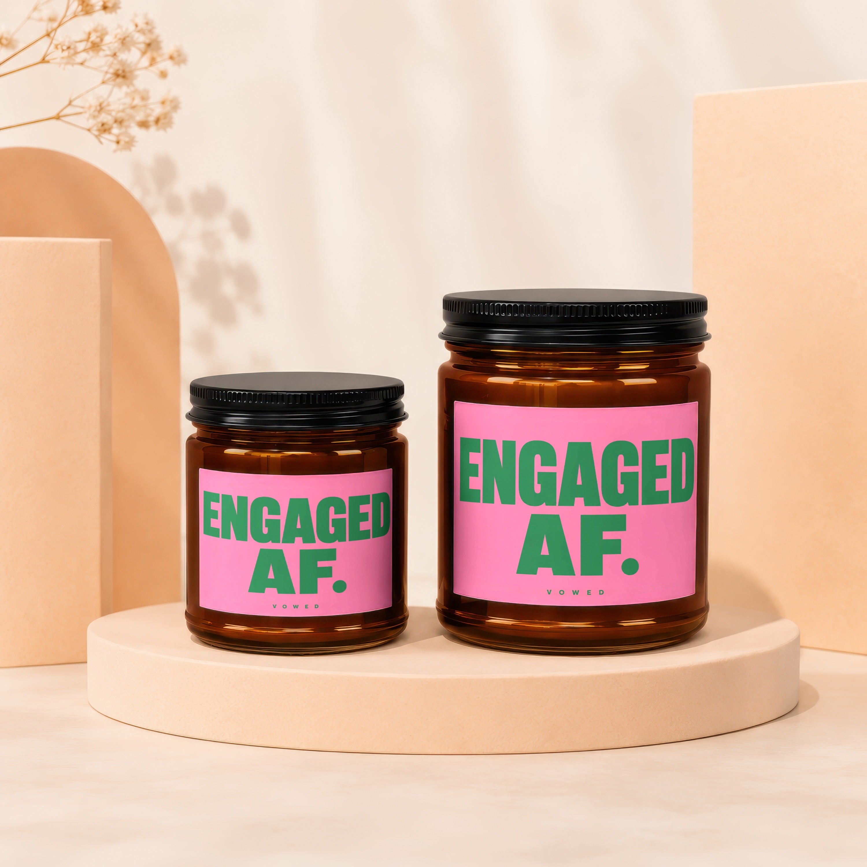 Two amber glass candles with pink labels reading "ENGAGED AF. VOWED"