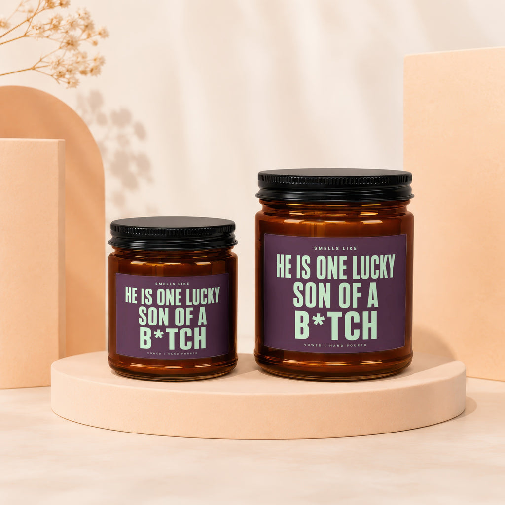 Two amber glass candles with black lids, featuring purple labels with light green text.