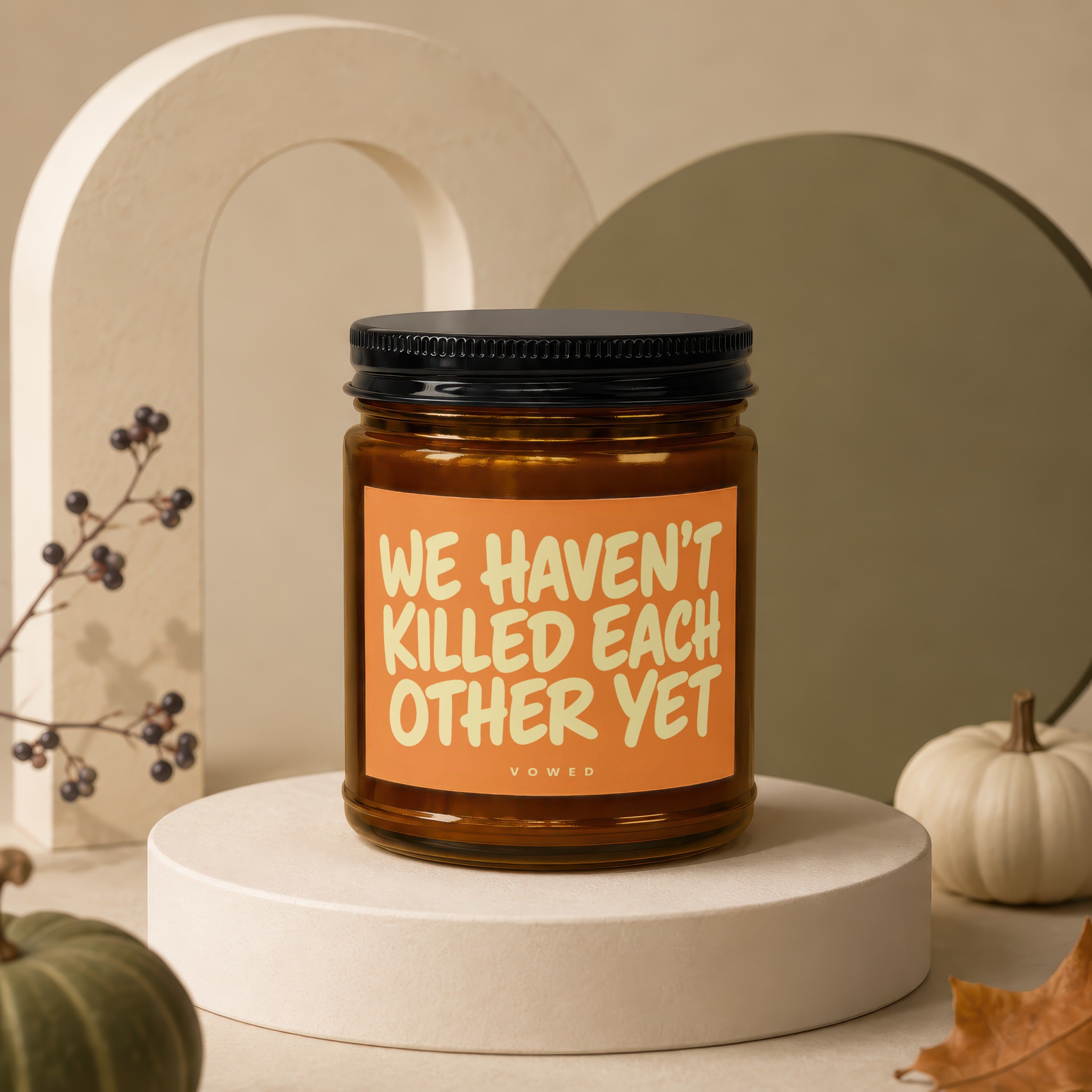 Amber jar candle with black lid displaying "WE HAVEN'T KILLED EACH OTHER YET" text.
